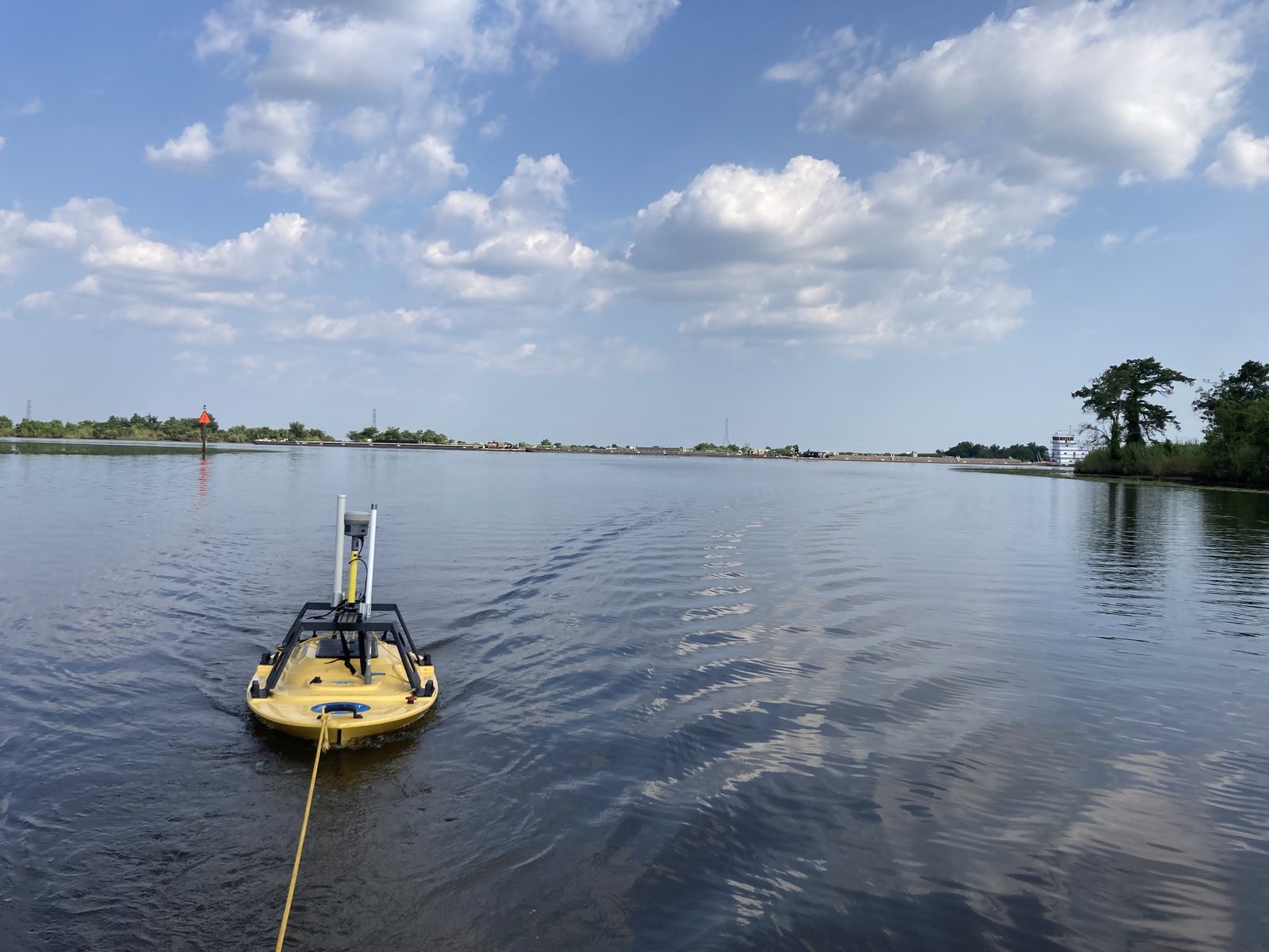 A small field vessel operating on open water near industrial shoreline conditions.